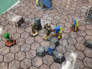 A close up shot of a Battletech map. Visible mechs from left to right: Assassin getting a rear armour shot on a Commando (visible far right), my Ostscout capturing an objective, a Wolfhound (top) firing on my Assassin (they miss), my Charger charging into a Nightsky. Finally, the Commando is getting a rear armour shot on my Spartan.