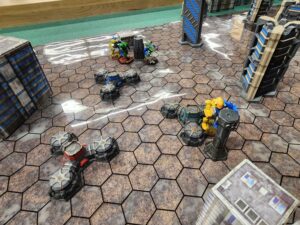 A photo of a Battletech Map, showing a Bushwacker capturing a point, my Assassin using AECM to turn the point off (preventing it from scoring) and also surviving a rear armour shot from a Nightsky for its troubles. Also visible is a Berserker scoring the middle objective.